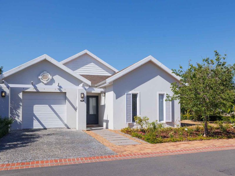A well-maintained single-story residential home featuring a paved driveway, single garage, and neat front garden with shuttered windows.
