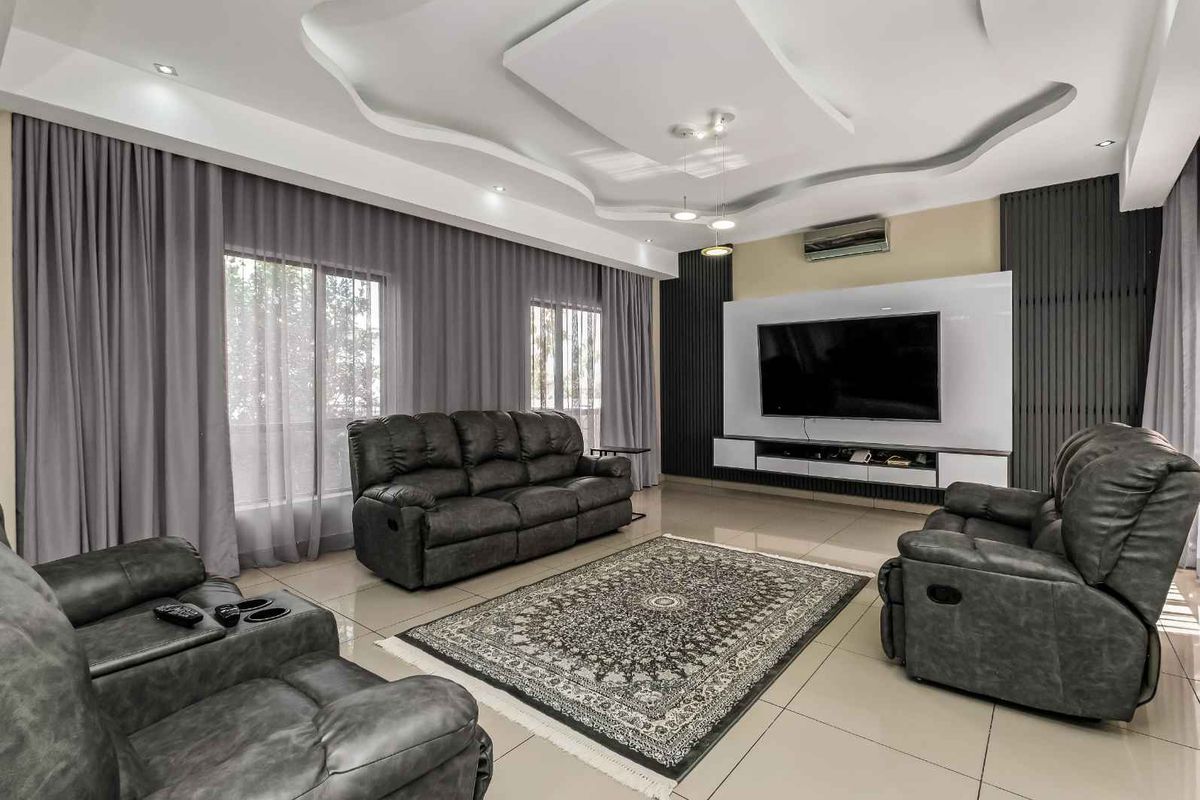 Modern living room featuring a decorative tray ceiling with recessed lighting, tiled flooring, and a built-in media wall unit.