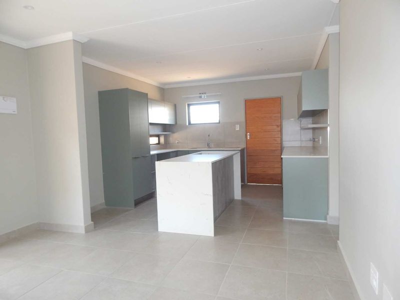 A modern, empty kitchen featuring a central island, sleek cabinetry, stone countertops, and neutral tiled flooring, offering a clean and contemporary space.