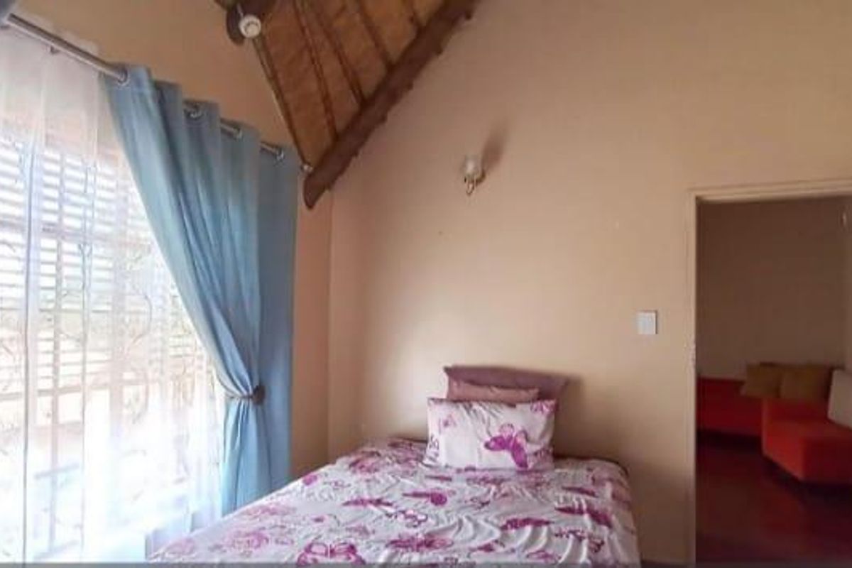 Bedroom featuring a high vaulted thatched ceiling, large window with natural light, and direct access to an adjoining living space.
