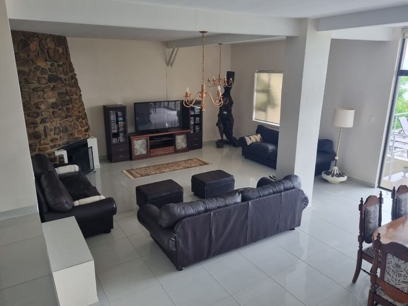 Spacious living area featuring a prominent stone fireplace, neutral tiled flooring, and direct access to an outdoor balcony through sliding glass doors.