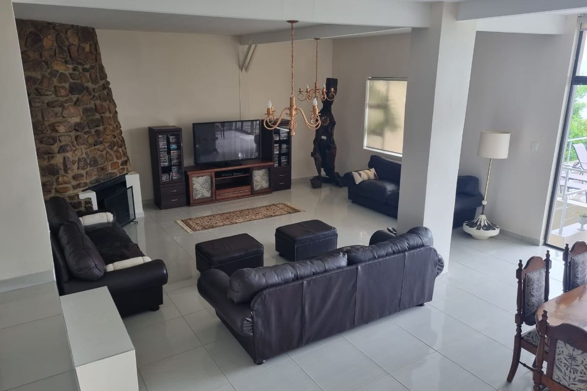 Spacious living area featuring a prominent stone fireplace, neutral tiled flooring, and direct access to an outdoor balcony through sliding glass doors.