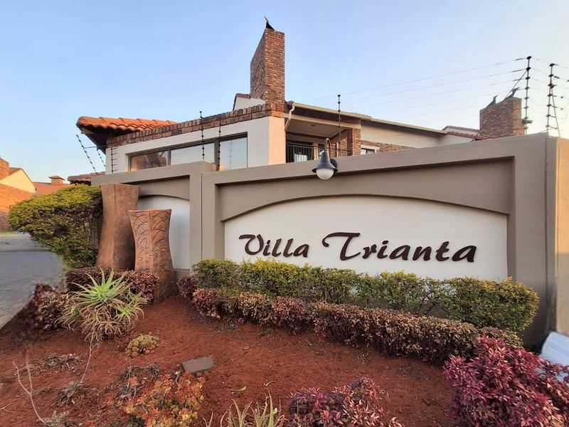 Front entrance view of Villa Trianta complex featuring a prominent boundary wall, electric fencing, and well-maintained landscaped garden area.