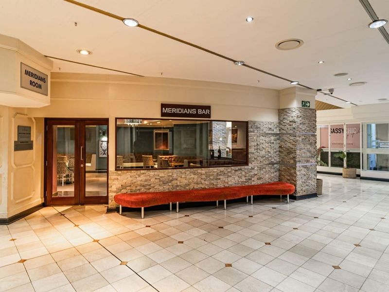 A view of the Meridians Bar entrance featuring stone-clad walls, tiled flooring, and recessed ceiling lighting within a commercial apartment building complex.