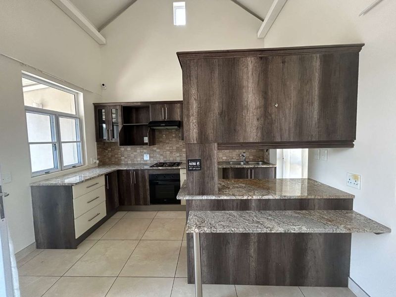 Modern kitchen featuring dark wood cabinetry, granite countertops, built-in oven, gas hob, and a breakfast bar under a high vaulted ceiling.