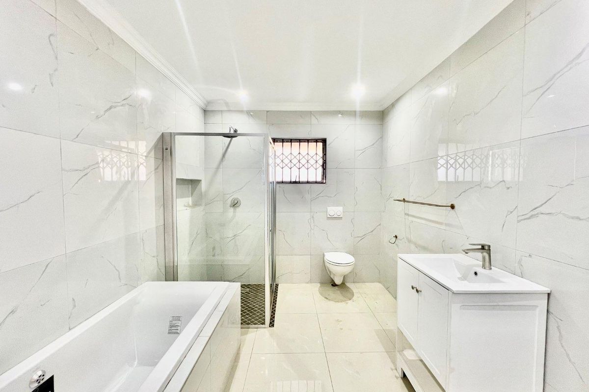 Modern bathroom featuring a bathtub, separate glass shower enclosure, wall-mounted toilet, and a vanity cabinet with marble-look wall tiles.
