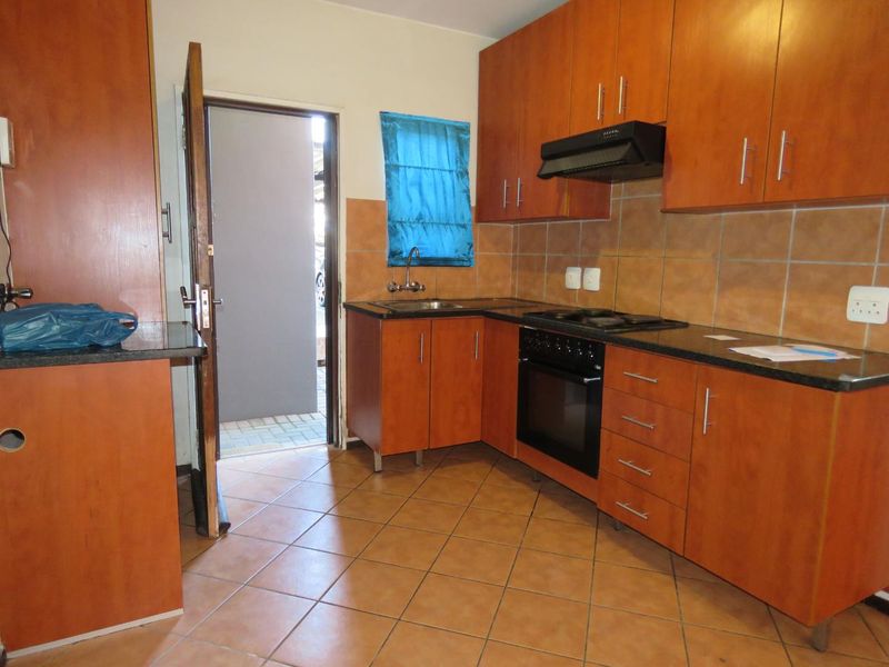 A functional kitchen featuring wooden cabinetry, granite countertops, built-in oven with hob, extractor fan, and tiled flooring, providing a practical workspace.