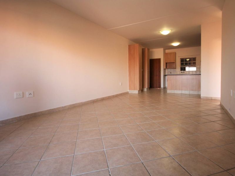 An open-plan living and kitchen area featuring tiled flooring, built-in cabinetry, and neutral walls, offering a versatile space ready for personalization.