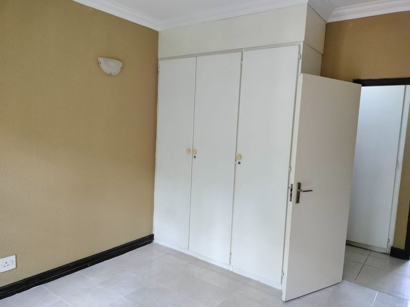 An empty bedroom featuring built-in cupboards, tiled flooring, and neutral wall tones, offering a blank canvas for personalization.