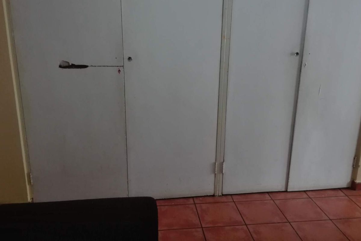 A bedroom featuring built-in cupboards with visible damage to one of the doors and tiled flooring.