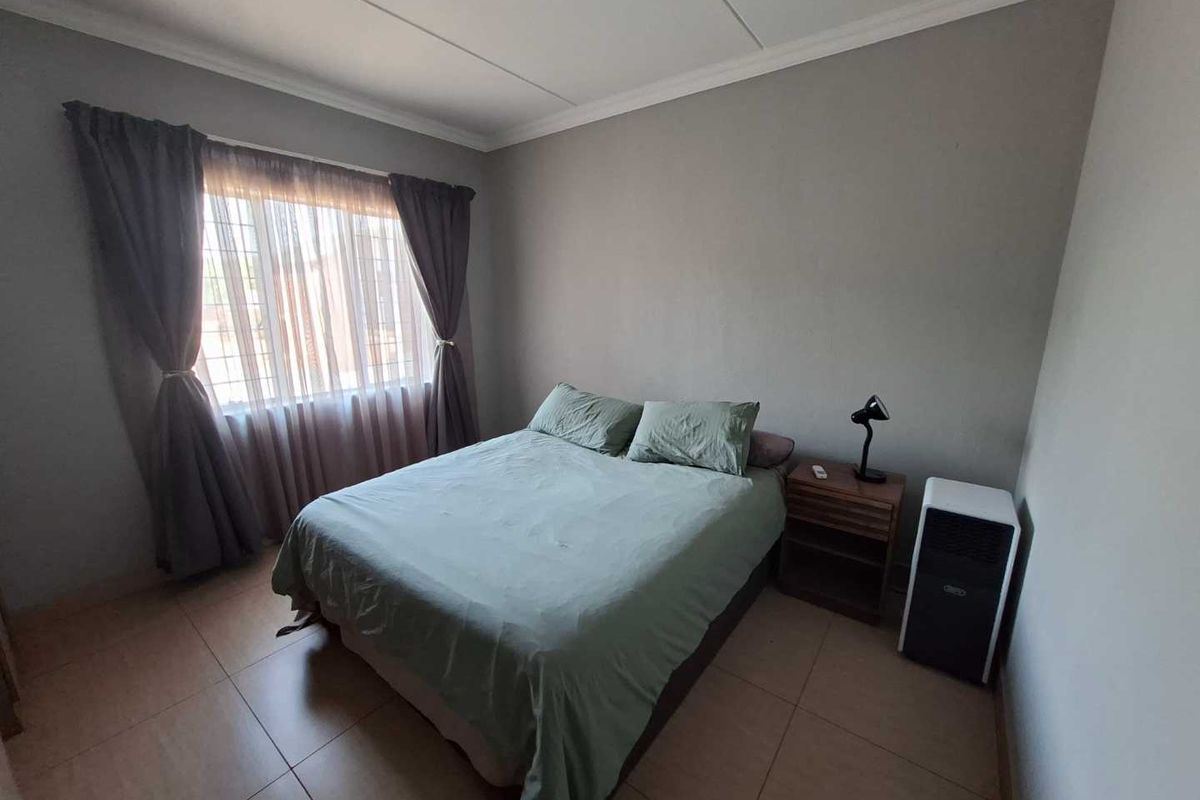 A well-lit bedroom featuring tiled flooring and a window with security bars, providing a functional and comfortable living space.
