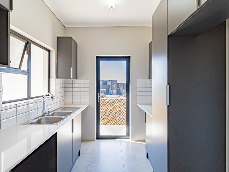 Modern scullery featuring sleek dark cabinetry, white quartz countertops, subway tile backsplash, and a double bowl sink with direct access to the exterior.