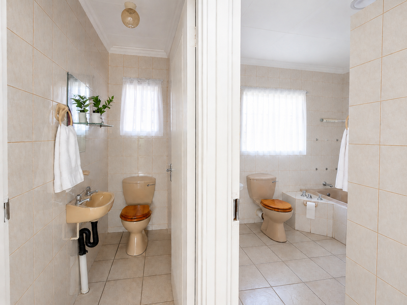 A functional bathroom suite featuring neutral ceramic tiling, a pedestal washbasin, a toilet, and a built-in bathtub with a tiled surround.