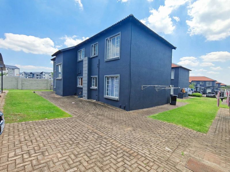 Rear view of a multi-story apartment building featuring dark blue exterior walls, tiled roofing, and paved ground area with surrounding lawn.