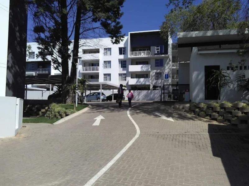 Front entrance view of a modern apartment complex featuring paved driveway access, covered parking bays, and multi-story residential units with balconies.