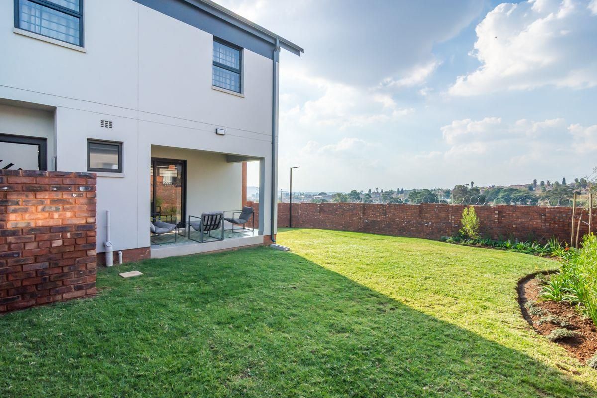 Rear view of the property featuring a private garden, brick boundary wall with security fencing, and a covered patio area.