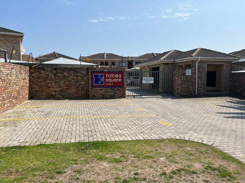 Front entrance view of the Times Square complex featuring a paved driveway, secure gated access, and brick perimeter walling with electric fencing.