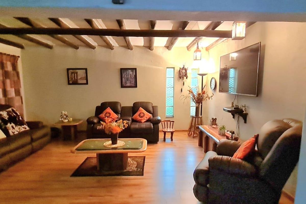A cozy living room featuring exposed timber ceiling beams, laminate flooring, and a unique vertical glass block window.
