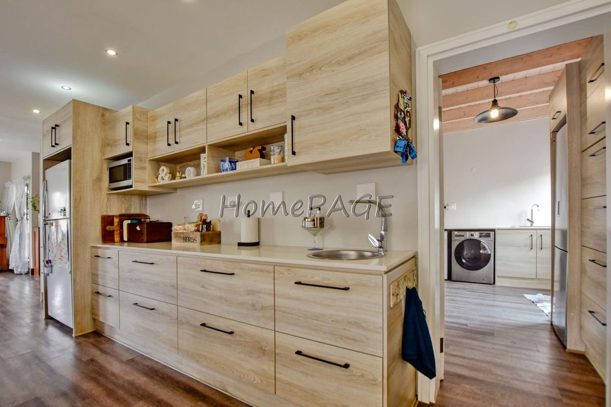 Modern kitchen featuring light wood-grain cabinetry, stone countertops, and integrated appliances, with a seamless transition to the adjacent laundry area.