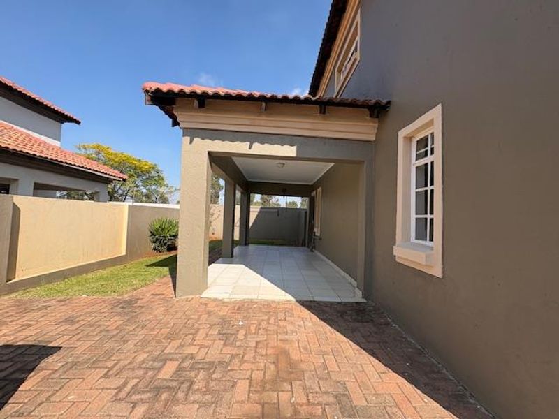 A covered patio area featuring tiled flooring, adjacent to a brick-paved outdoor space and enclosed by a boundary wall.