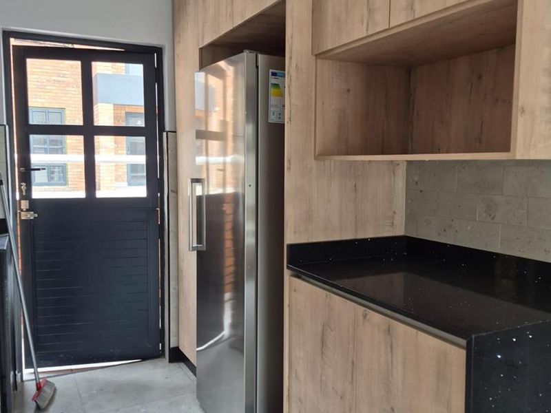 A functional scullery area featuring modern wood-look cabinetry, dark stone countertops, and tiled flooring with direct access to the exterior.