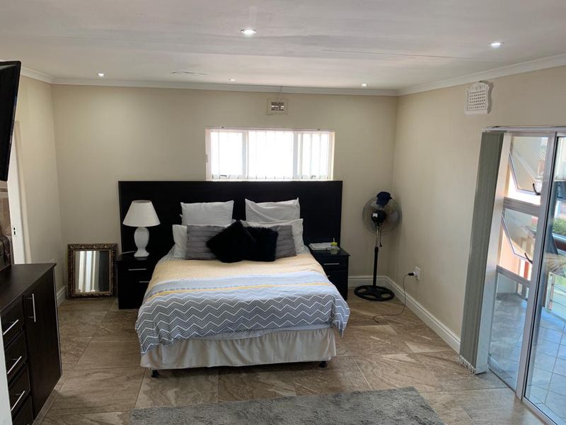 A spacious bedroom featuring tiled flooring, recessed downlighting, and a sliding glass door providing access to an outdoor area.