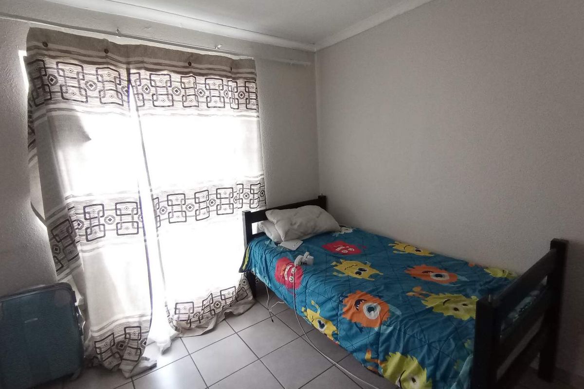 A functional bedroom featuring tiled flooring and a large window with natural light, providing a simple and practical living space.