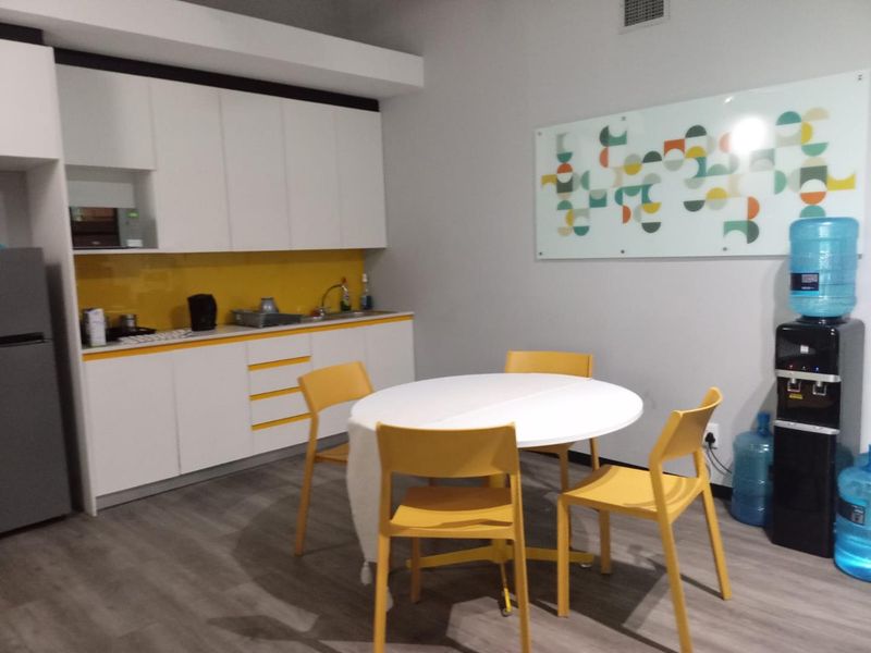 A functional office kitchenette featuring white cabinetry, a vibrant yellow glass splashback, and durable laminate flooring, suitable for staff breakroom use.