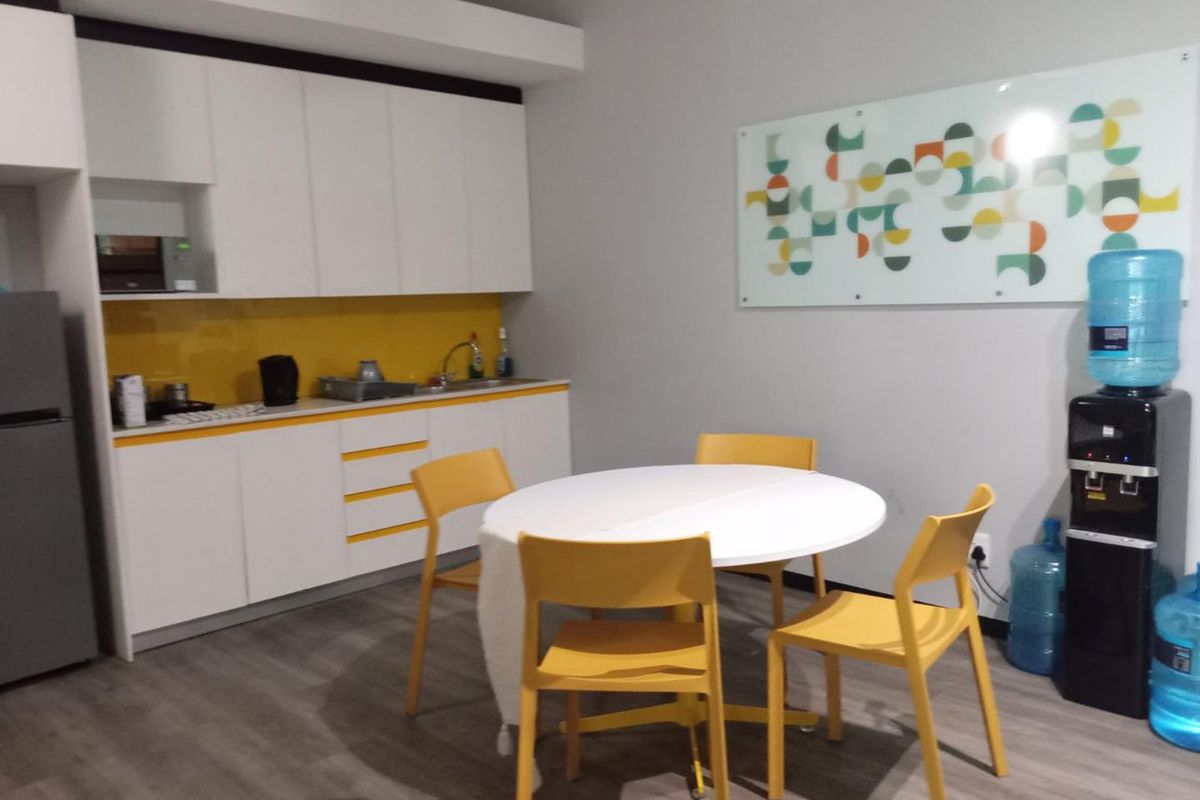 A functional office kitchenette featuring white cabinetry, a vibrant yellow glass splashback, and durable laminate flooring, suitable for staff breakroom use.