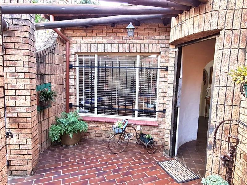 A covered patio area featuring face brick walls, tiled flooring, and a timber pergola structure, providing a sheltered entrance to the home.