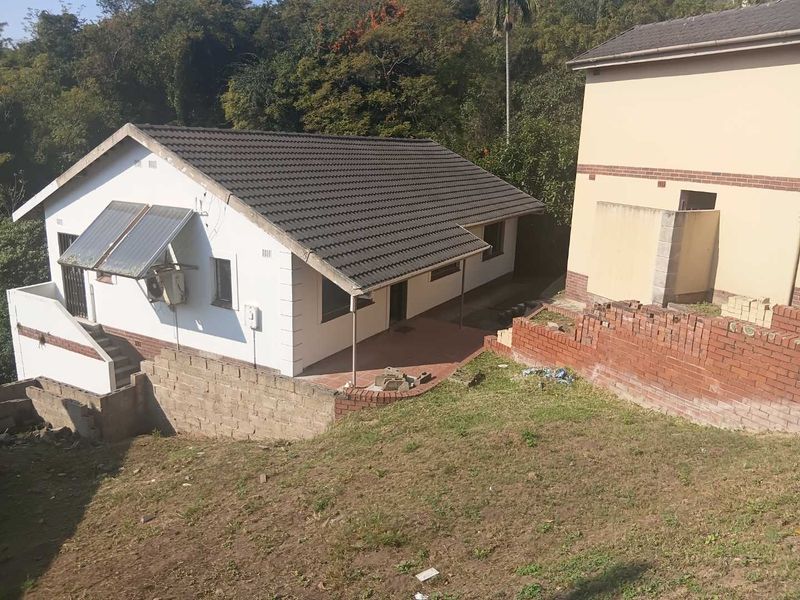 Rear view of the property featuring a tiled roof, solar water heating system, and a covered patio area with adjacent brick retaining walls.