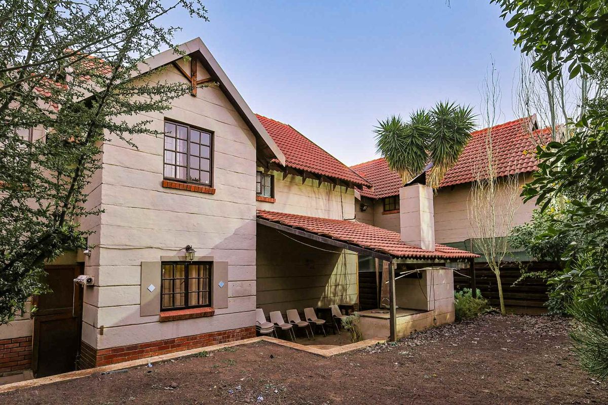 Rear view of the townhouse featuring a covered patio with a built-in braai, tiled roof, and established garden space.