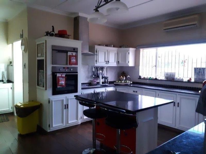 A functional kitchen featuring white cabinetry, a central island with a dark countertop, built-in oven and microwave, and a wall-mounted air conditioning unit.