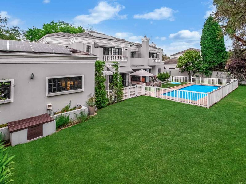 Rear view of the property featuring a well-maintained lawn, a fenced swimming pool, and a multi-level exterior with solar panels on the roof.