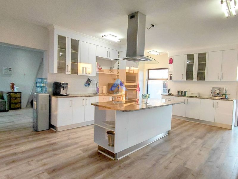 Modern kitchen featuring white cabinetry, granite countertops, a central island with an extractor fan, and light-toned laminate flooring.