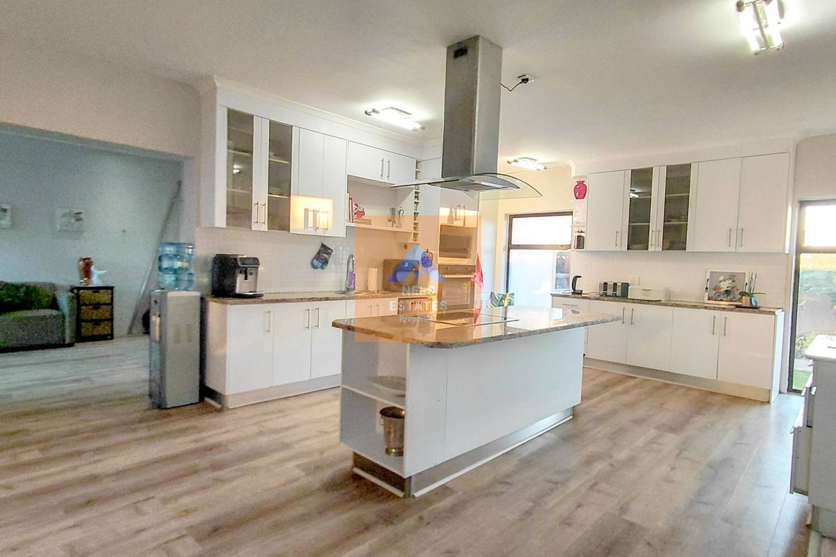 Modern kitchen featuring white cabinetry, granite countertops, a central island with an extractor fan, and light-toned laminate flooring.