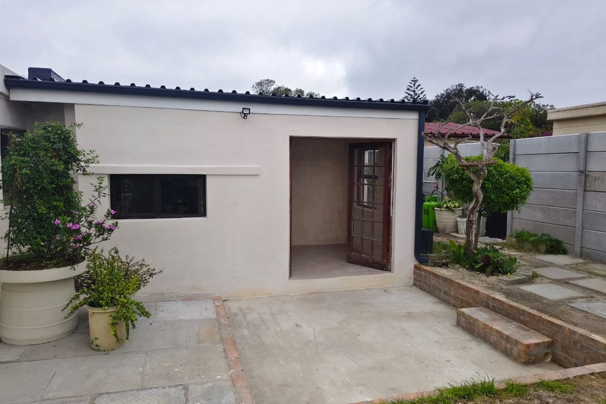 A rear view of the cottage featuring a concrete patio area, a single glass-paneled door, and a small window, set within a private garden space.