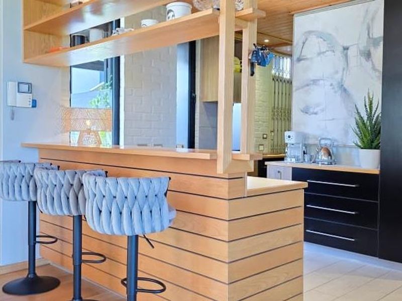 Modern kitchen featuring a timber breakfast bar, open shelving, and sleek built-in cabinetry with a warm timber ceiling finish.