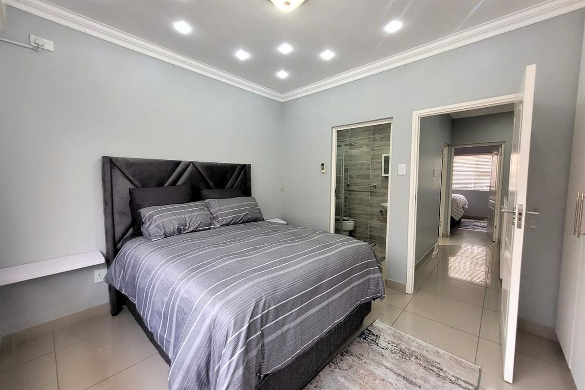 A well-maintained bedroom featuring tiled flooring, recessed ceiling lighting, and an en-suite bathroom with a glass-enclosed shower.