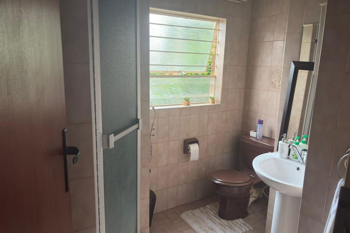 A functional bathroom featuring a pedestal sink, toilet, and shower enclosure with neutral wall and floor tiling.