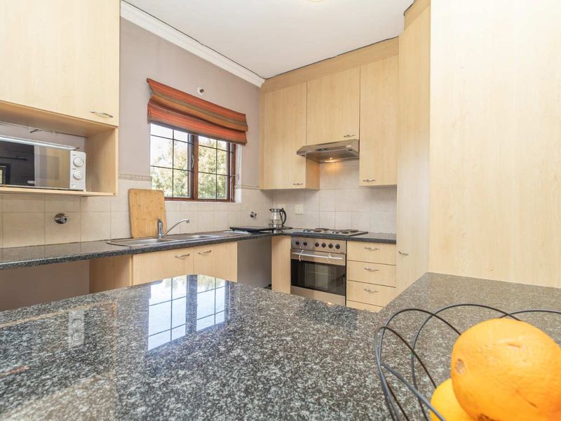 Functional kitchen featuring light wood cabinetry, granite countertops, built-in oven, gas hob, and a tiled backsplash with a window for natural light.