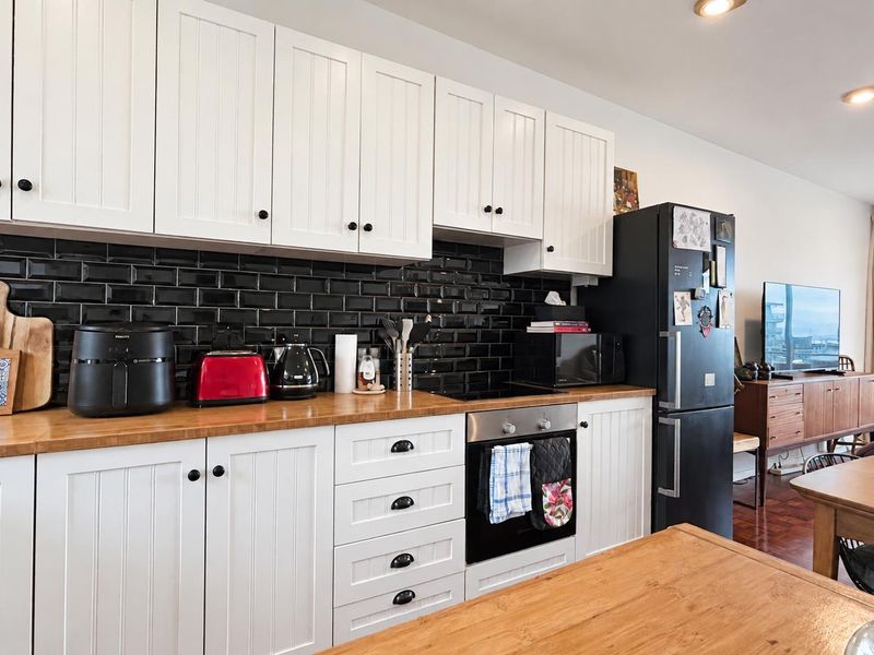 Open-plan kitchen featuring white shaker-style cabinetry, a contrasting black subway tile backsplash, and warm wooden countertops, seamlessly flowing into the living area.