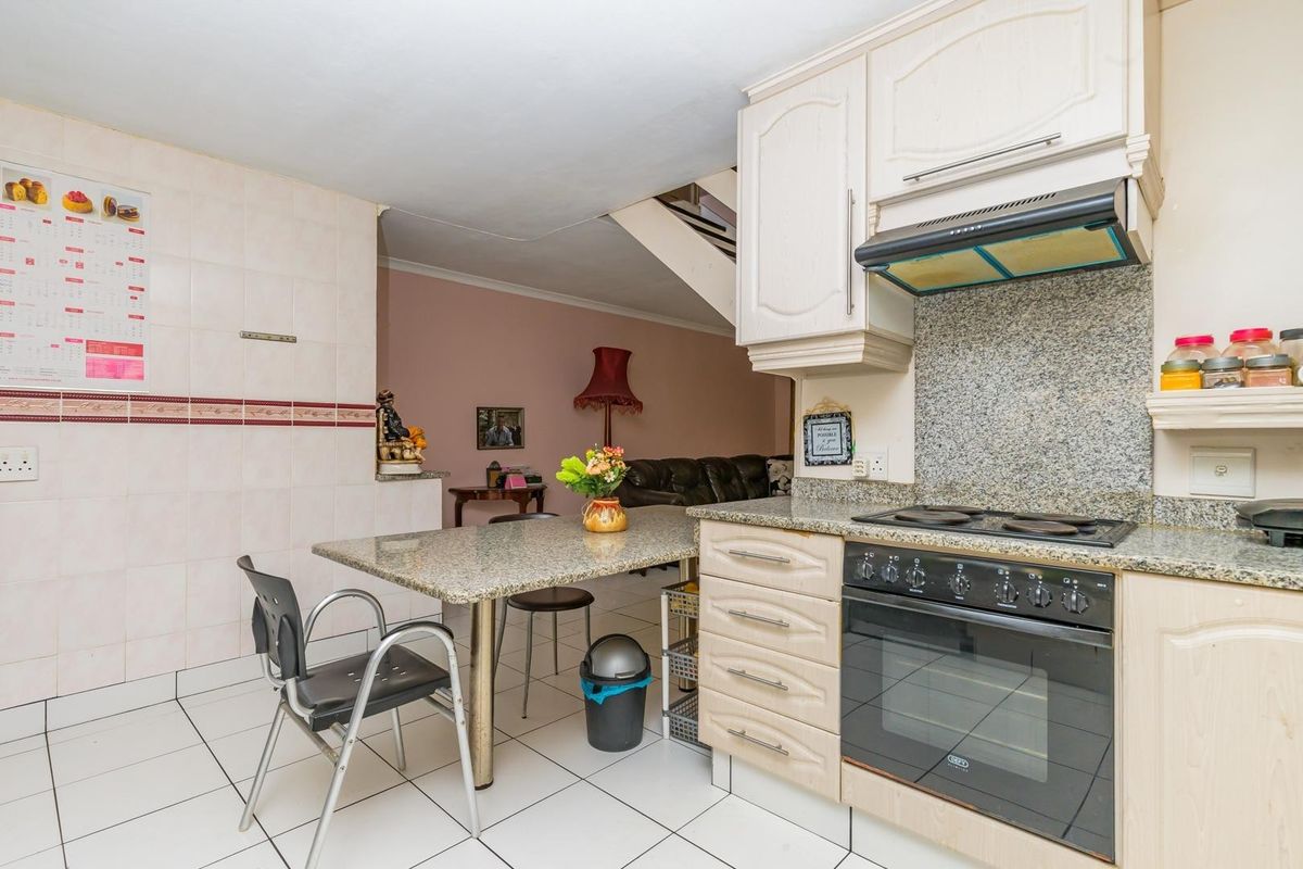 A functional kitchen featuring granite countertops, built-in cabinetry, an integrated oven and hob, and tiled flooring, with an open-plan layout leading to the living area.