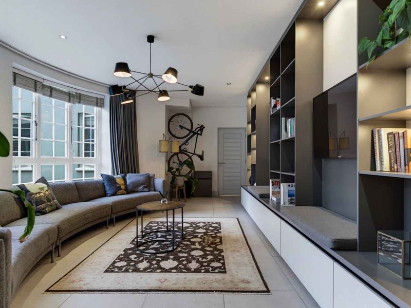 Modern living room featuring extensive built-in shelving and cabinetry, large multi-pane windows, recessed lighting, and sleek tiled flooring.