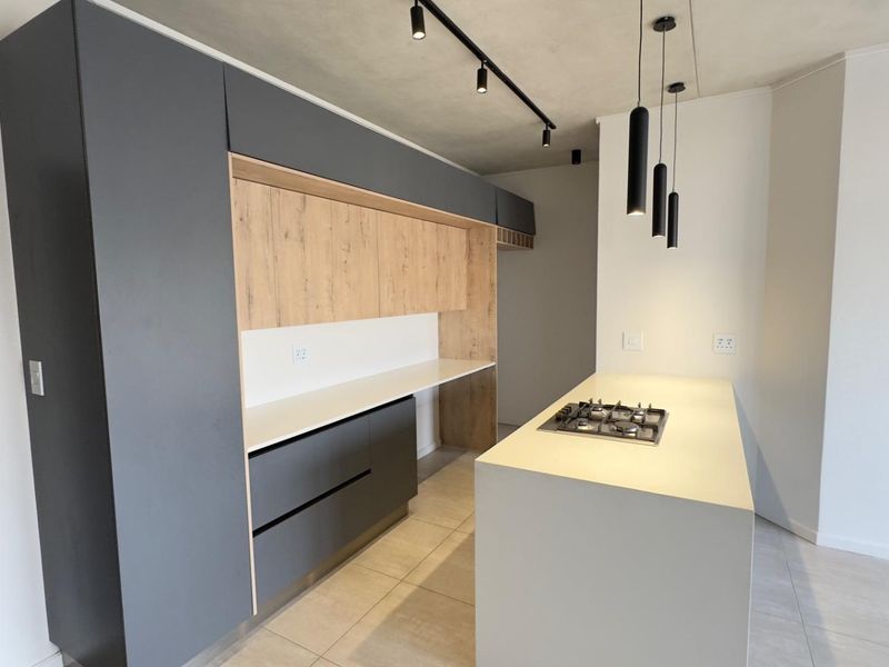 Modern kitchen featuring sleek grey and wood-grain cabinetry, stone countertops, a central island with a gas hob, and contemporary track and pendant lighting.