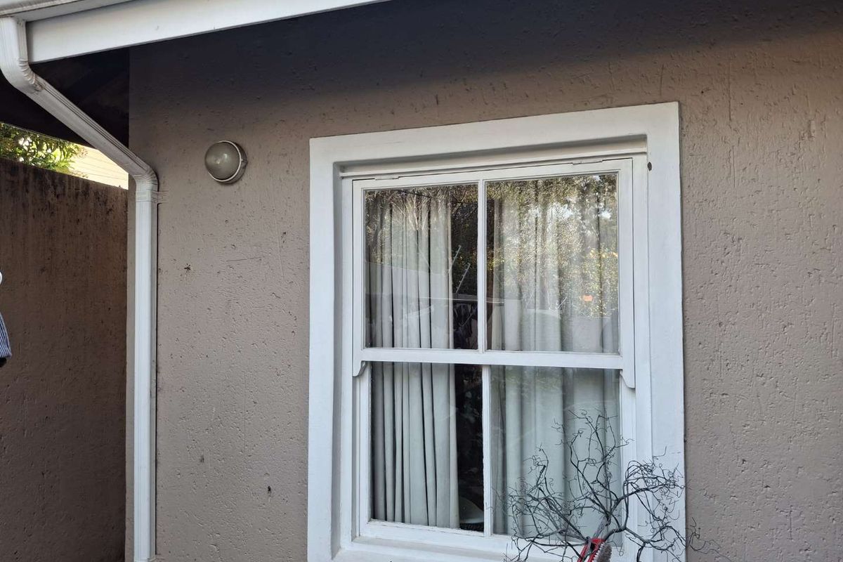 A view of the exterior rear wall featuring a white-framed sash window, guttering, and an exterior wall light.