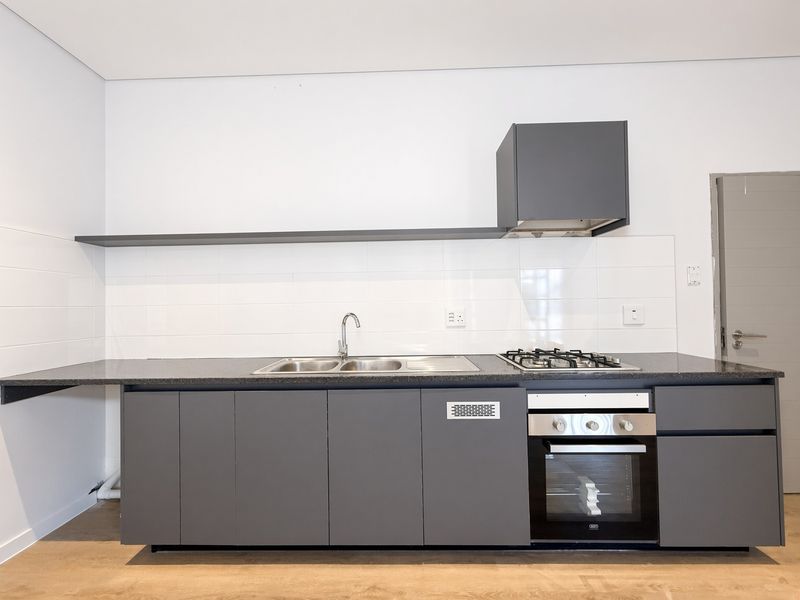 Modern kitchen featuring sleek grey cabinetry, built-in oven, gas hob, extractor fan, and a stainless steel sink with a clean tiled splashback.