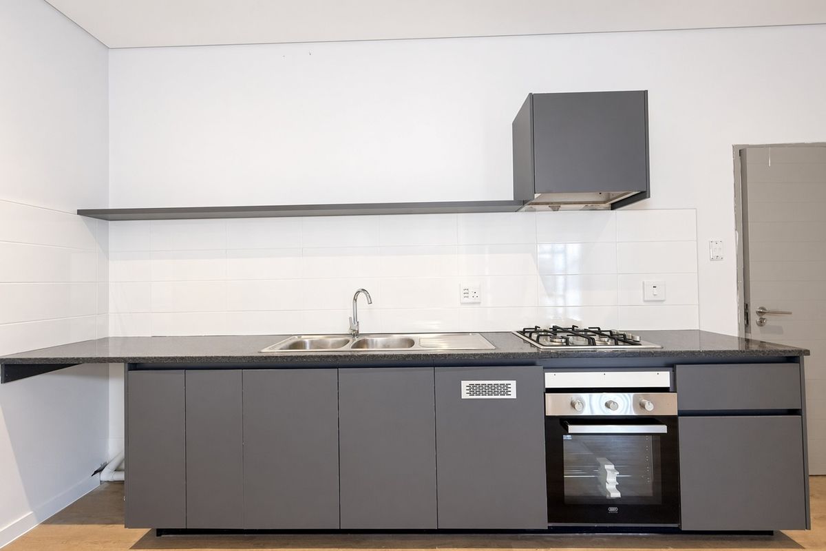 Modern kitchen featuring sleek grey cabinetry, built-in oven, gas hob, extractor fan, and a stainless steel sink with a clean tiled splashback.