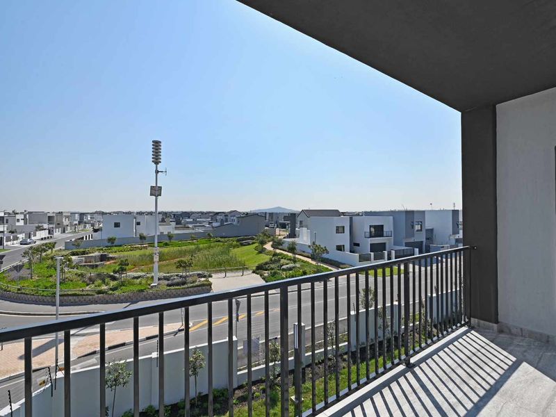 A modern apartment balcony featuring a metal balustrade and concrete flooring, offering an elevated view of the surrounding residential estate.
