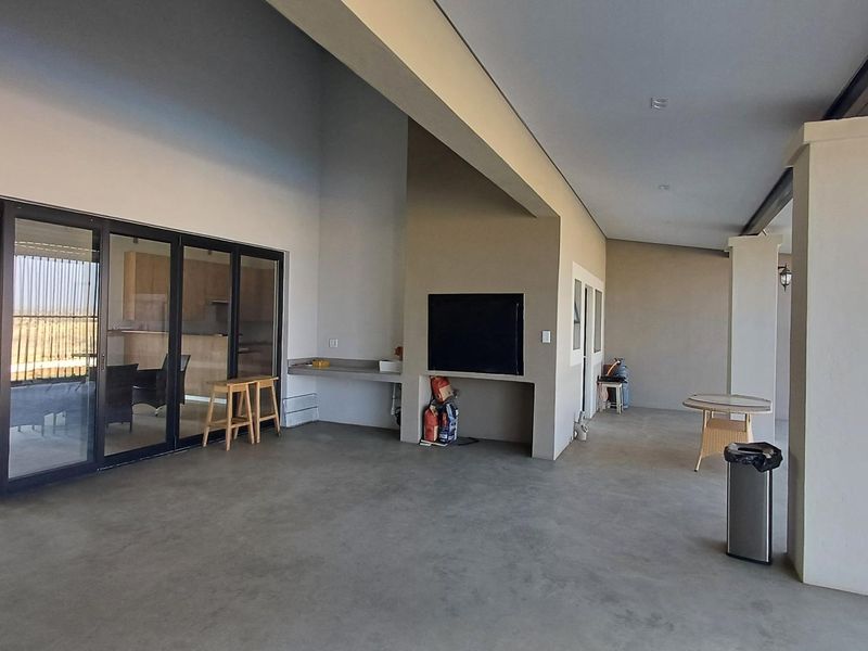 Spacious covered patio featuring a built-in braai, concrete flooring, and large sliding glass doors providing seamless access to the interior living space.